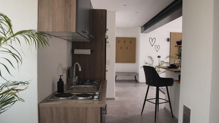 Een moderne keuken met houten meubels en een klein kookgedeelte. De ruimte is licht en modern ingericht met planten en een gezellig zithoekje.