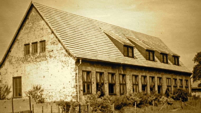 Un vieux bâtiment rustique avec un toit en pente et plusieurs fenêtres. L'image présente un aspect sépia qui lui confère une touche nostalgique.