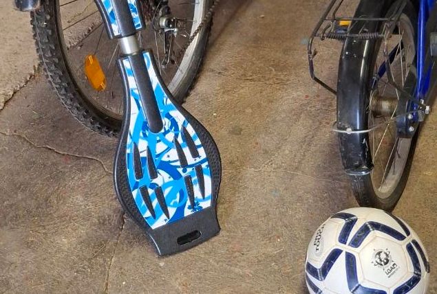 Een skateboard met een blauw ontwerp staat naast fietsen en een voetbal. De vloer is van beton en vertoont slijtage.