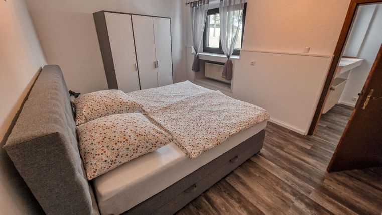 Ein gemütliches Schlafzimmer mit einem großen Bett und Holzfußboden. Es gibt einen Kleiderschrank und ein Fenster mit Vorhängen.
