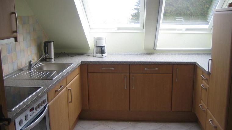 A modern kitchen with wooden cabinets and a bright countertop. Large windows let in plenty of light.