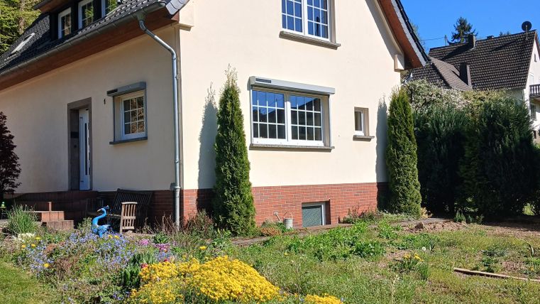 Ein schönes Haus mit einem gepflegten Garten. Die Blumen blühen in bunten Farben und die Sonne scheint.