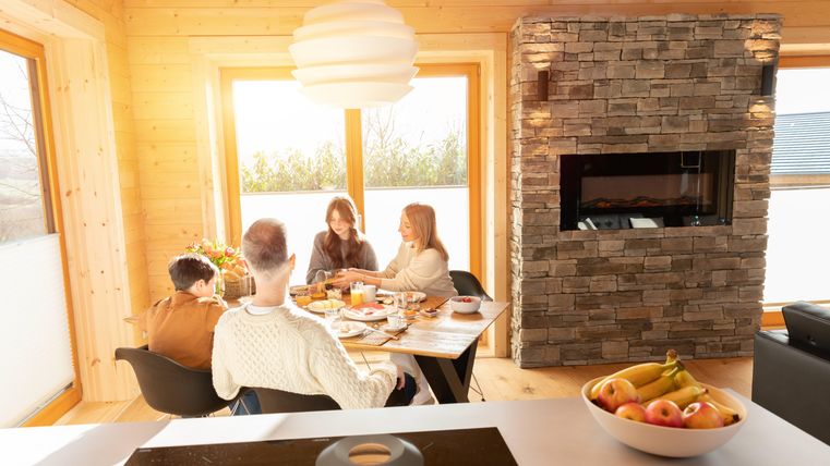 Ein gemütlicher Essbereich mit vier Personen, die gemeinsam am Tisch sitzen. Die Atmosphäre ist freundlich und hell, mit großen Fenstern und einem modernen Kamin.