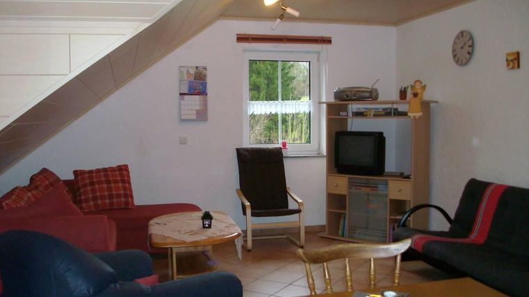 Een gezellige woonkamer met verschillende zithoeken en een tafel. Er is een televisie en een raam met uitzicht naar buiten.