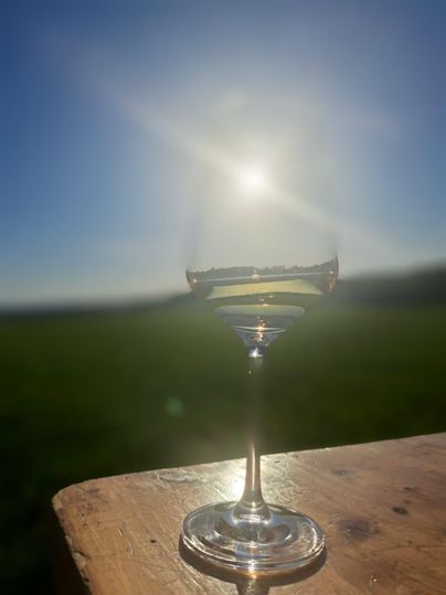 Ein elegantes Weinglas steht auf einem Holztisch. Im Hintergrund strahlt die Sonne in einem klaren blauen Himmel.