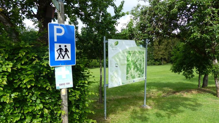 Un panneau de parking pour les randonneurs à côté d'un panneau d'information dans un environnement boisé et verdoyant.