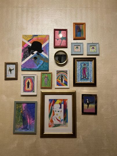 Un mur avec différentes images et peintures dans des cadres colorés. Les motifs montrent de l'art abstrait et figuratif.