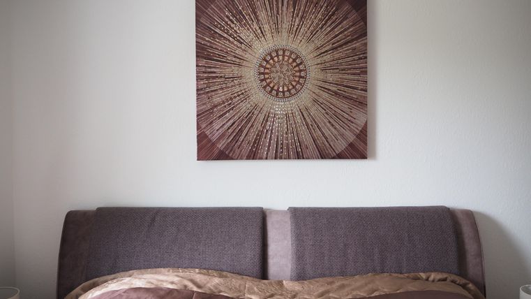 Ein gemütliches Schlafzimmer mit einem großen Betthaupt und einer dekorativen Wandkunst. Die Farben sind warm und einladend.