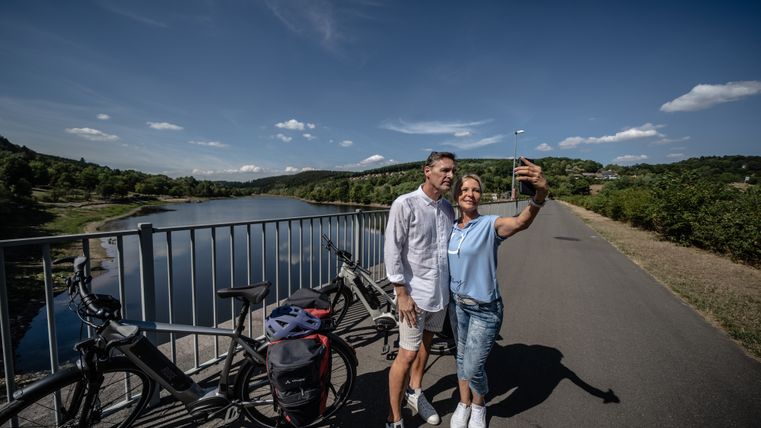 Een koppel neemt een selfie op een brug aan het Kronenburger Meer, met fietsen op de achtergrond.