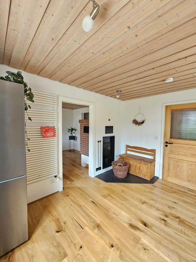 Een moderne keuken met houten vloeren en houten plafonds. Aan de muur staat een koelkast en er is een open haard en een gezellige zithoek.