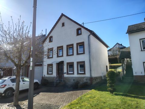 A freestanding house with white walls and brown window frames. In front of the house is a green lawn and a walkway.