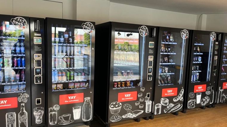 Eine Reihe von Snack- und Getränkeautomaten in einem hellen Raum. Die Automaten sind mit verschiedenen Produkten und einem modernen Design ausgestattet.