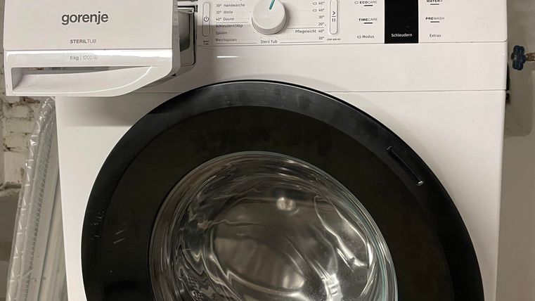 Eine moderne Waschmaschine steht an der Wand. Darüber befindet sich ein Wäschekorb und ein kleiner Aufbewahrungskorb.