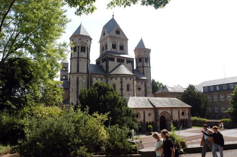 Une église historique avec plusieurs tours, entourée d'espaces verts. Au premier plan, on peut voir quelques visiteurs explorer les environs.