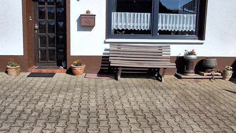 Een modern huis met een witte gevel en browne kozijnen. De oprit is geplaveid en er staat een bankje voor de voordeur.