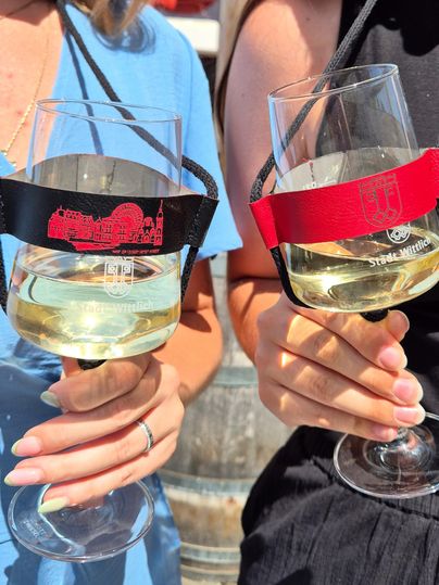 Twee personen houden wijnglazen in de hand. De glazen hebben een gekleurde houder en bevatten elk een lichte drank.