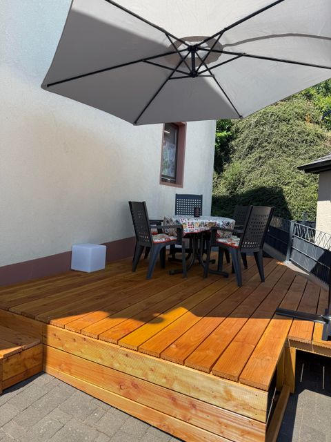 Une terrasse confortable avec un parquet en bois et un grand parasol. Une table ronde avec des chaises invite à la détente.