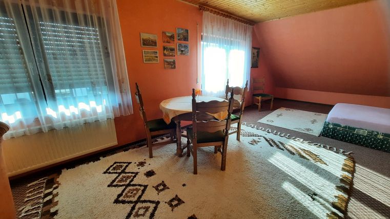 Une chambre confortable avec des murs orange et une table ronde. Il y a des chaises, un tapis et beaucoup de lumière naturelle provenant des fenêtres.