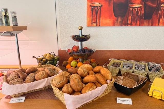 A buffet with various types of bread in baskets. Fruit in a bowl and cutlery on a tray are also visible.