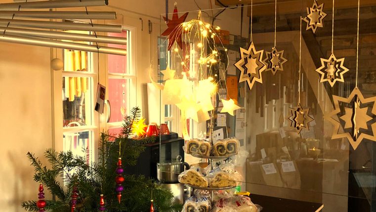 Eine festliche Weihnachtsdekoration mit hängenden Sternen und Lichtern. Auf dem Tisch stehen Kekse und ein kleiner Weihnachtsbaum.