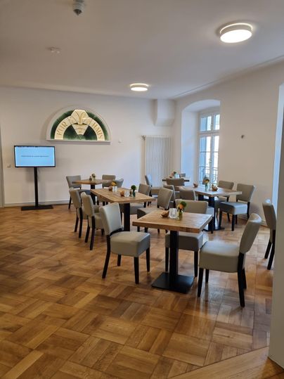 An elegant dining room with wooden floors and several tables. There is space for guests, and a screen is available.