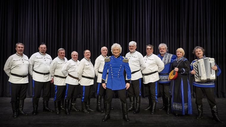 Een groep mensen in traditionele klederdracht staat samen op een trap. Ze glimlachen en poseren voor de foto.
