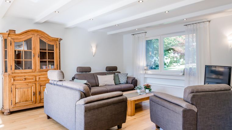 Een gezellige woonkamer met een grijs bank en twee stoelen. Ook te zien zijn een houten kast en een raam met uitzicht op het groen.