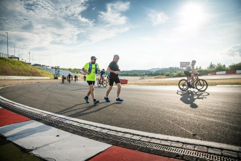 Sporting activity on a racetrack with runners and cyclists. The sun is shining and the sky is partly cloudy.