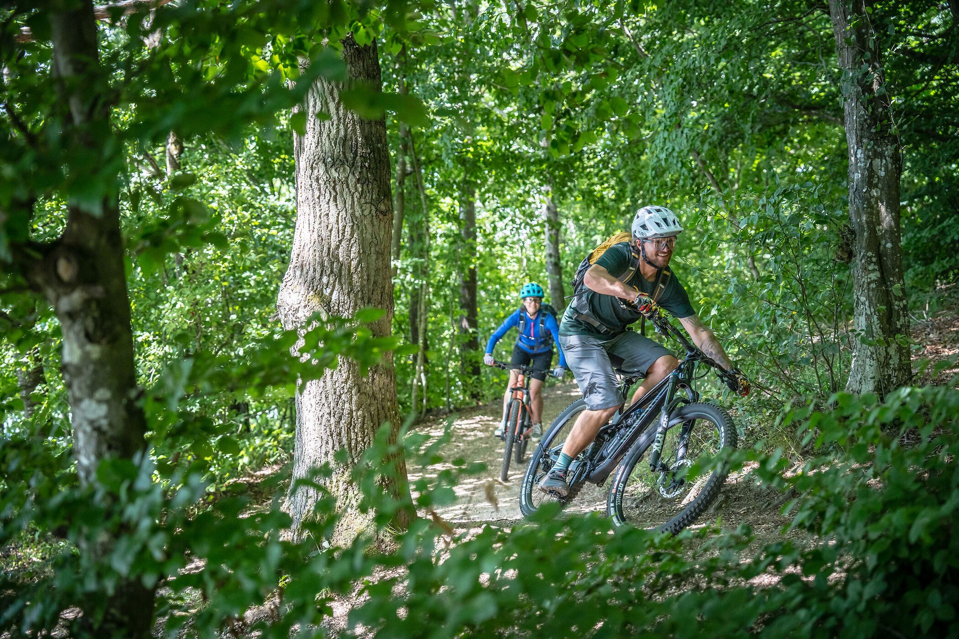 Ein Mann und ein Frau fahren zügig mit dem Fahrrad um eine Kurve im Wald