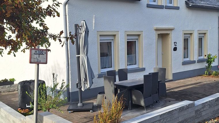 Een verzorgd huis met een lichte verf en een kleine voortuin. De straat is rustig met een heldere blauwe lucht op de achtergrond.