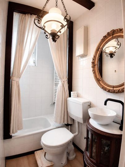 A small bathroom with a bathtub, a sink, and a toilet. Elegant elements like a mirror and a lamp give the room charm.