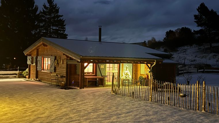 A cozy wooden cabin in the snow at night. The light from the windows creates a warm atmosphere.