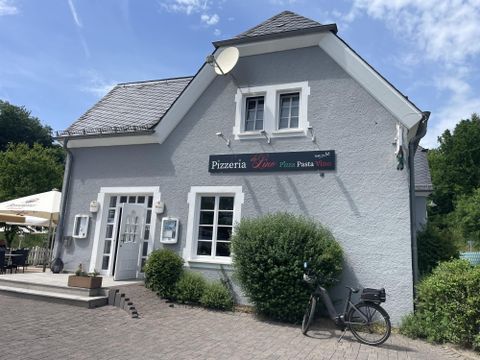 Een gezellige pizzeria met een grijze gevel en een uitnodigende ingang. Voor het gebouw staan een fiets en enkele planten.