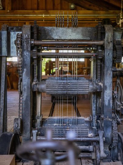 Eine alte Webmaschine aus Metall steht in einem rustikalen Raum. Sie zeigt die mechanischen Teile und Fäden, die für die Stoffherstellung verwendet werden.