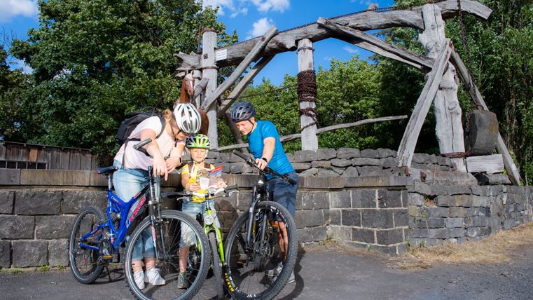 Une famille à vélo étudie une carte devant un vieil équipement minier en bois à l'extérieur.