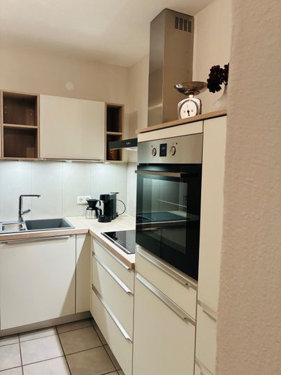 Een moderne keuken met witte kasten en een ingebouwd fornuis. De ruimte is licht en ruim, met tegelvloeren en een kraan.