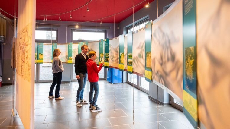 Een tentoonstelling in een ruimte met meerdere informatieposters. Bezoekers bekijken de kunstwerken en interageren met de exposities.