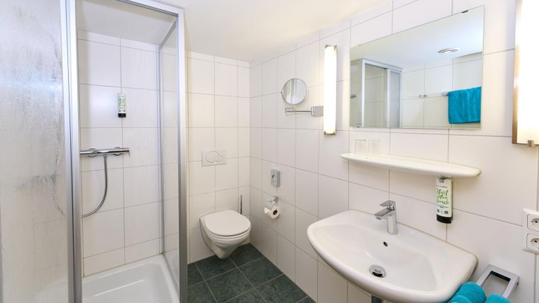 Een moderne badkamer met douche en wastafel. De muren zijn betegeld en er zijn handdoeken in een frisse blauwe kleur.