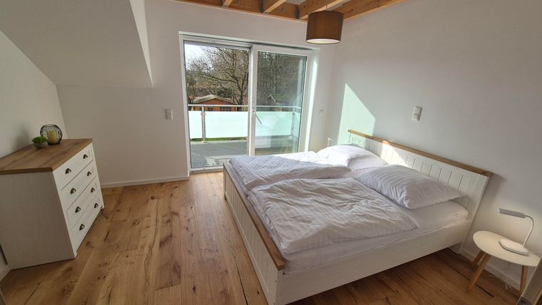 Une chambre lumineuse avec un grand lit et un sol en bois. De grandes fenêtres laissent entrer beaucoup de lumière naturelle et offrent une belle vue.