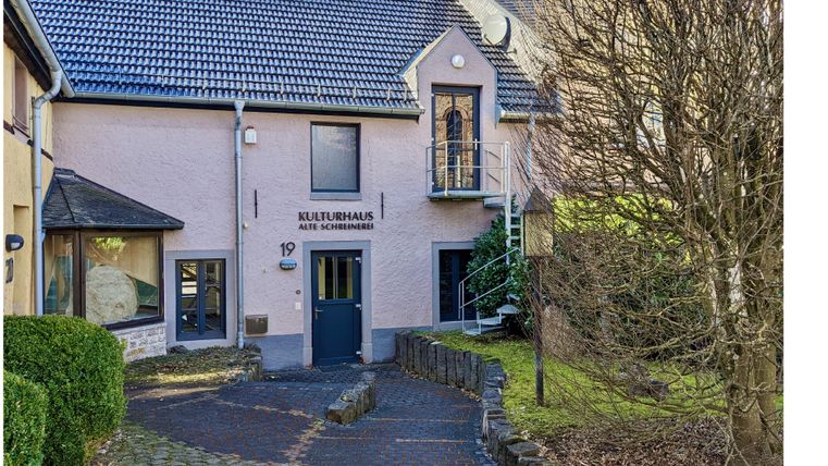 Buitenfaçade van het cultuurhuis in Hillesheim met een klein gras- en plantenhoekje voor de ingang.