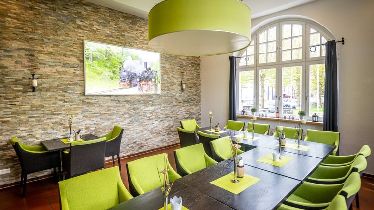 Ein modernes Restaurant mit einem eleganten Design. Die Tische sind mit grünen Stühlen und minimalistischen Dekorationen ausgestattet.