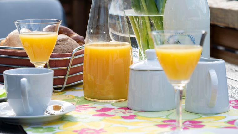 Een gedekte tafel met verse fruitsap, koffie en gebak. De kleurrijke tafelkleed zorgt voor een uitnodigende sfeer.