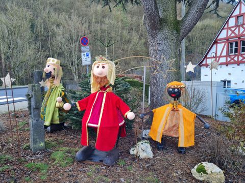 Drei Figuren der Heiligen Drei Könige in bunten Gewändern stehen im Freien vor einem Baum.