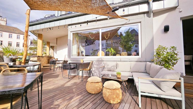 A modern terrace with cozy seating and wooden flooring. Covered by a sunshade, the space creates an inviting atmosphere.