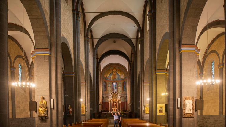 A beautiful church interior with high vaults and wooden benches. In the background, there is an altar with religious images.