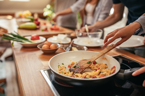 Mensen die samen koken - Een persoon houdt een lepel in de hand, een andere persoon snijdt groenten - ontspannen sfeer