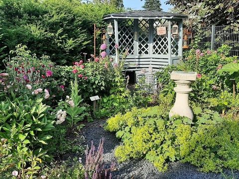 Ein schöner Garten mit bunten Blumen und grünen Pflanzen. Im Hintergrund steht eine gemütliche Pergola.
