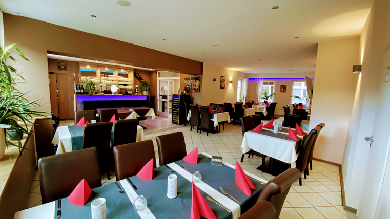 Een uitnodigend restaurant met een elegante inrichting. De tafels zijn gedekt met witte tafelkleden en rode servetten.