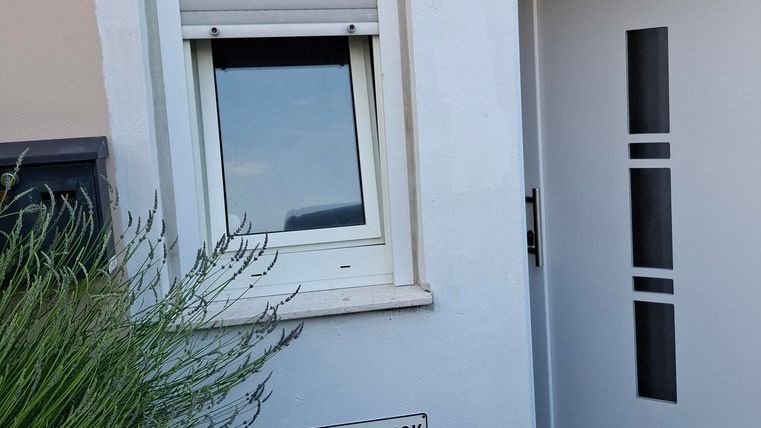A modern house with a clear, white entrance area and a window. In front of the house stands a sign with the inscription "Phaus Waldblick".