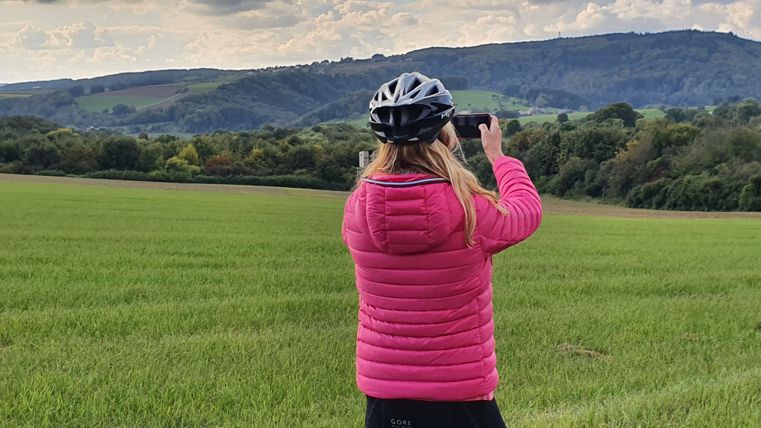 Person mit pinker Jacke und Fahrradhelm fotografiert Landschaft.